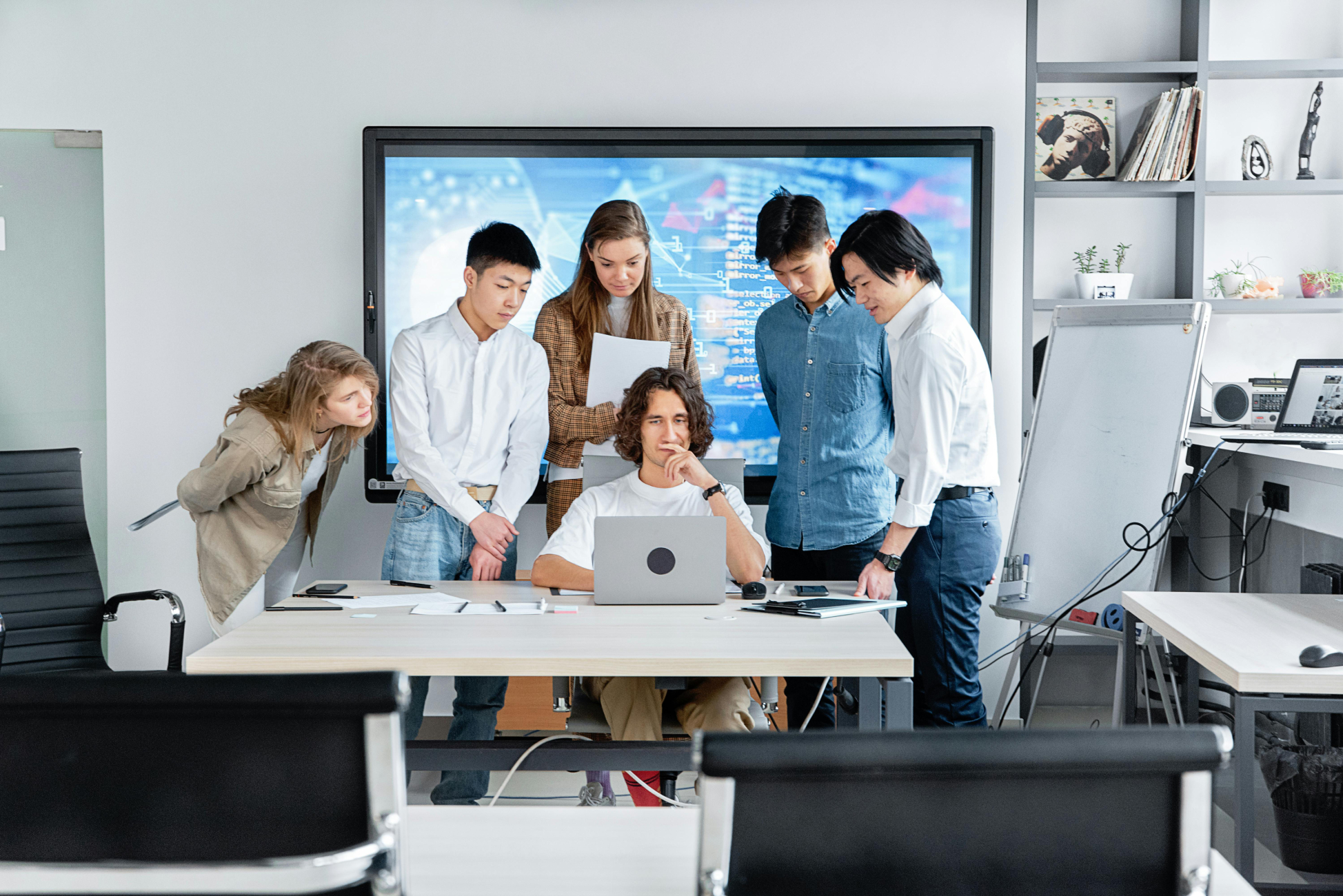 Diverse IT team collaborating at modern office workspace using data visualization screens