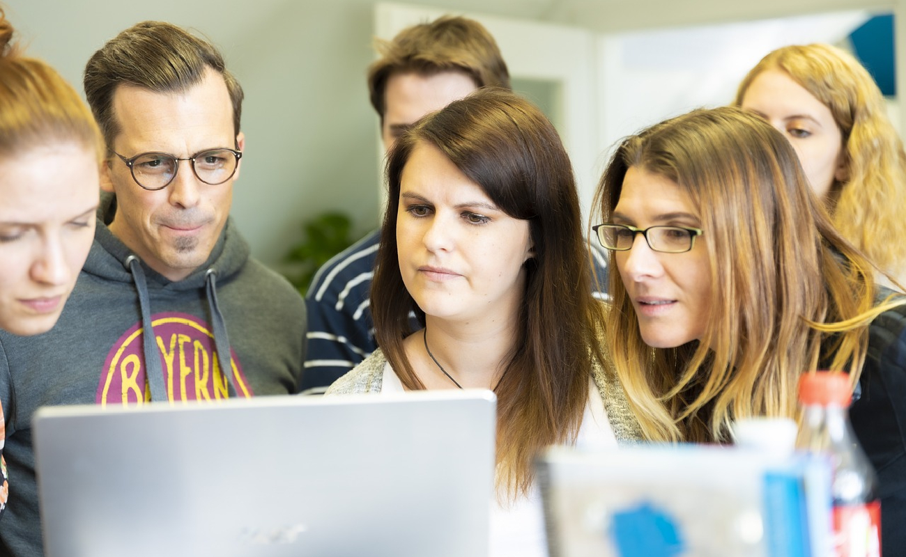 A diverse group of professionals closely collaborating on a laptop, symbolizing teamwork and problem-solving in modern IT environments.